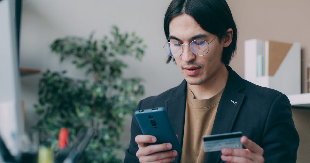 Businessman in office attire using a smartphone and holding a credit card, focusing on online payment process.